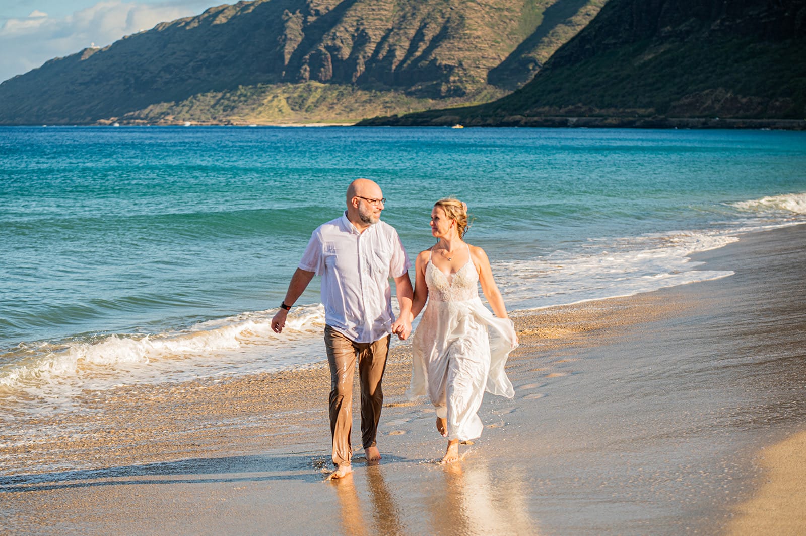 A couple walking the shoreline on the North Shore of Oahu, green mountains behind