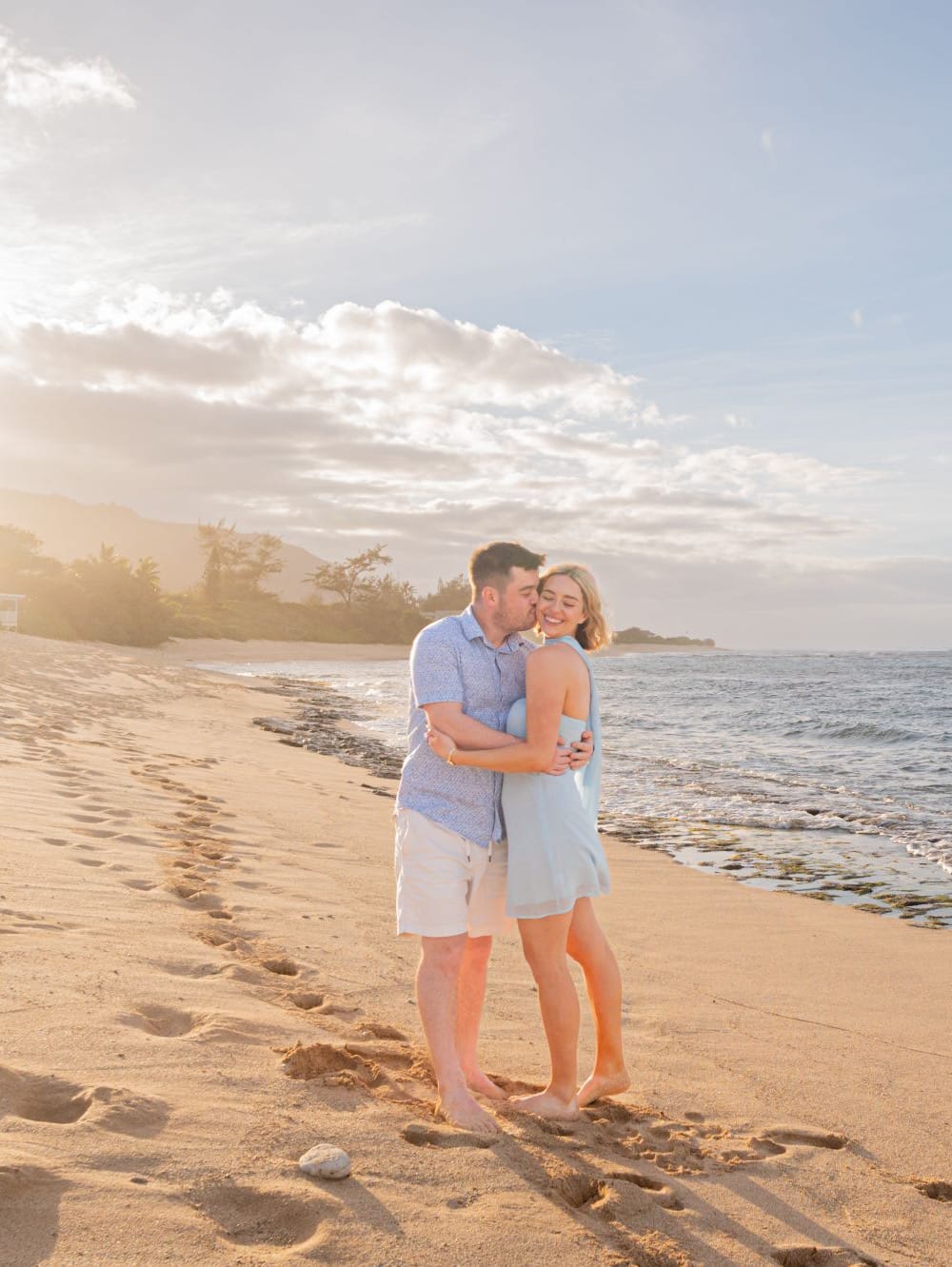 A couple on Mokuleia Beach at sunset, the sun on the water behind them