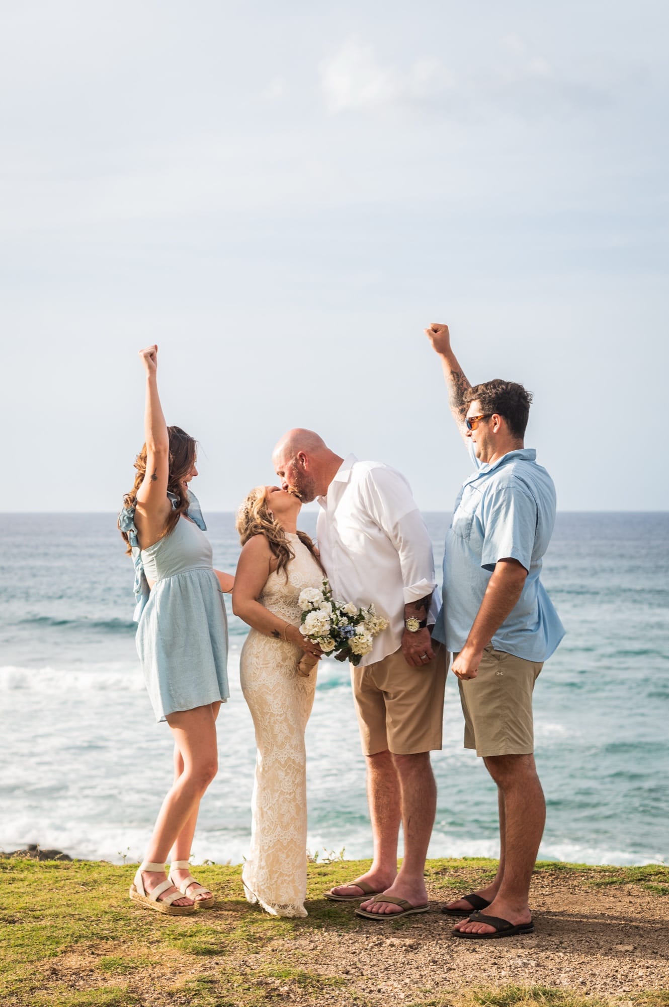 Two friends cheering as a couple kisses on a cliff above the ocean on the North Shore of Oahu