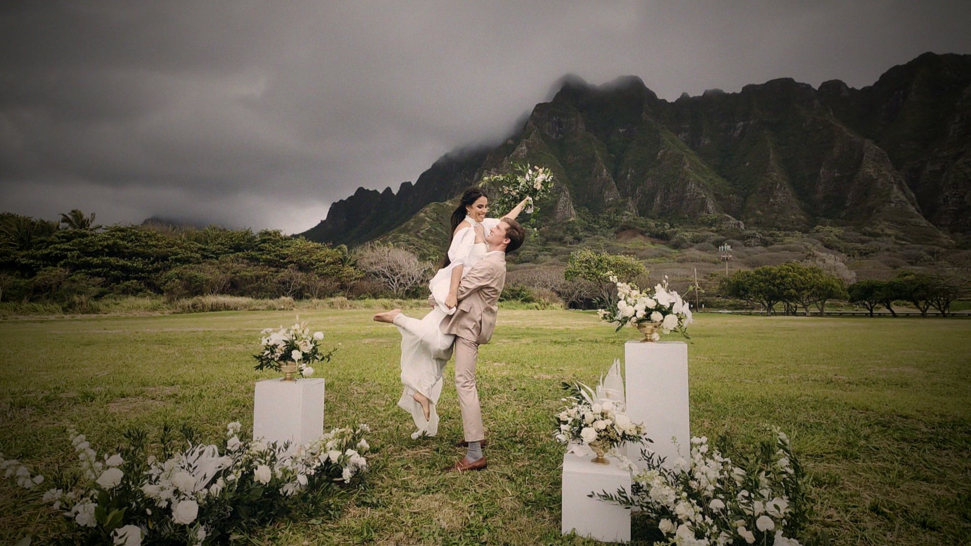 A couple lifted in a spin at their Oahu elopement ceremony at Kualoa, the mountains behind them